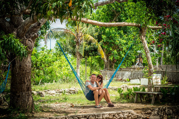 Portrait of a happy young romantic couple trying to sit together in a hammock during their vacation on the tropical island Bali, Indonesia. Love scene. Asia.