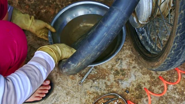 closeup Vietnamese woman in gloves squats cleans motorcycle inner tube to fit patch in repair shop