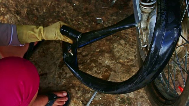 closeup Vietnamese woman in gloves squats sinks into water motorcycle inner tube checks air leakage in repair shop