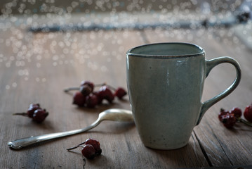 Blaue Tasse auf Holztisch mit Löffel und Hagebutten
