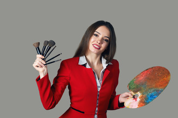 Fototapeta premium Cheerful beautiful young woman, the makeup artist on a gray background , with brush in hand