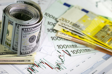 Concept of currency exchange trading. Roll of Hundred us dollar bills standing . Piles of euro bills. Currency us eur exchange chart under the bills. 200 euro bills, 100 euro fan shaped.
