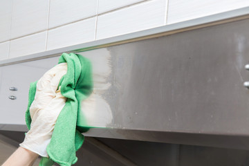 Hand in protective glove with rag cleaning kitchen equipment in the professional kitchen. Stainless steel surface. Early spring cleaning or regular clean up.