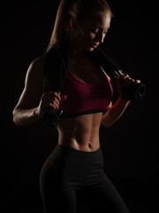 Fototapeta na wymiar Sexy and strong athletic young woman with slim gorgeous body and collected hair wearing the sportswear is posing over dark black background in the studio, sweat on the abdominal, fitness