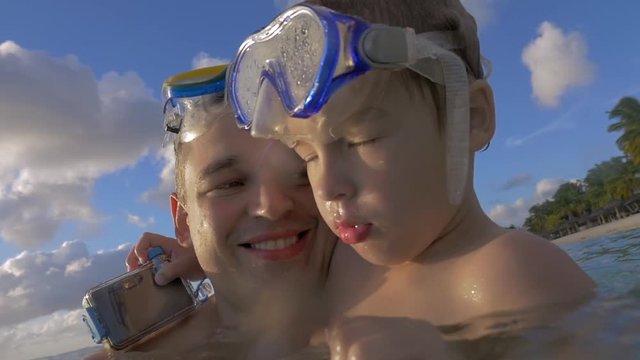 Slow motion view of happy young father with son in the water in snorkeling masks against blue cloudy sky, father kisses son, Port Louis, Mauritius Island