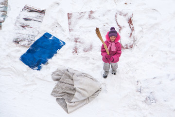 Cute little girl cleaning mats and rugs with a broom on a snow f