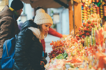 Young beautiful woman selecting holiday candies on Christmas market