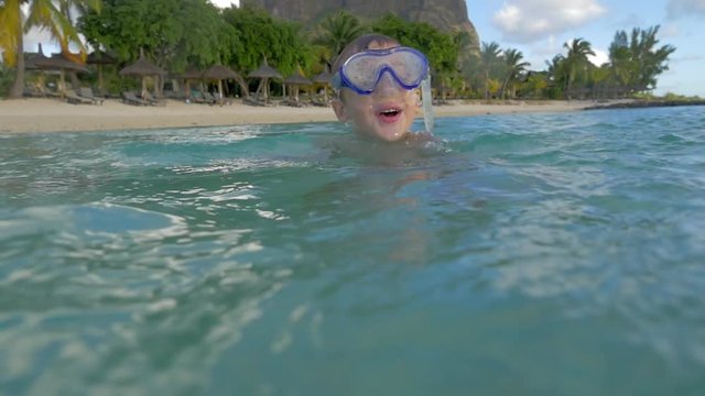 Slow motion view of small boy swimming in the blue water of Indian Ocean in the snorkeling mask near beach and then take a picture using one way waterproof camera, Port Louis, Mauritius Island