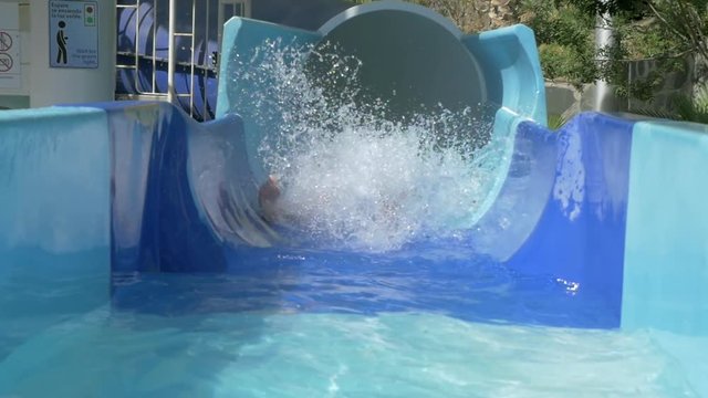 Slow motion shot of a woman appearing from the tube slide in outdoor water park. Having fun on water attractions
