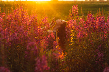 Beautiful girl in profile on field, sun backlight, sunrise, orange colors, hands near the neck