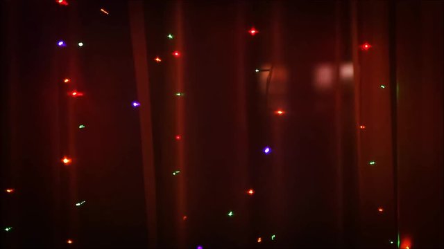 Christmas lights in the window on the background of transparent tulle.