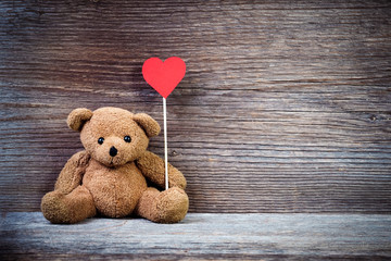 Teddy bear with heart sitting on old wood background.