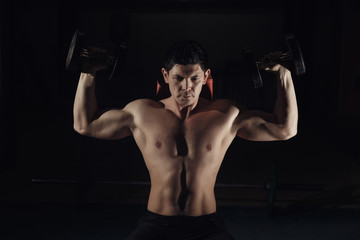 Fototapeta na wymiar Muscular man training his shoulders with dumbbells.