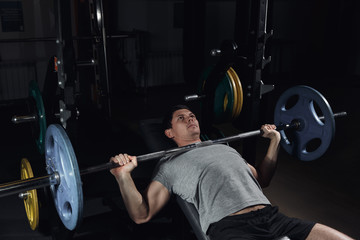 Weight lifter at the bench press lifting a barbell on an incline bench.