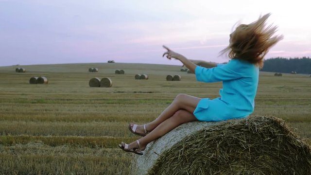 Beautiful young woman sitting on a haystack and dancing.