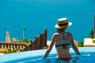 Young slender woman in pool enjoy vacation and looking at Dead Sea. View from behind. 2017 New Travel season concept. Copyspace.