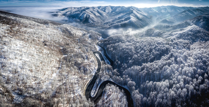 Panoramic image of a winding road from a high mountain pass in Transylvania, Romania with snow covered mountains in the background