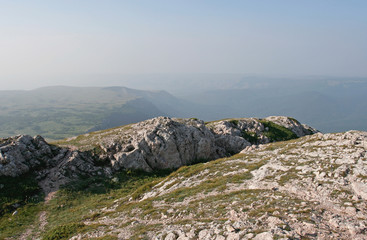 Fototapeta na wymiar The mountain landscape with small white limestone rocks, green savin and distant mountains. This photo was taken in mountainous massif Chatyr-Dag, Crimea.