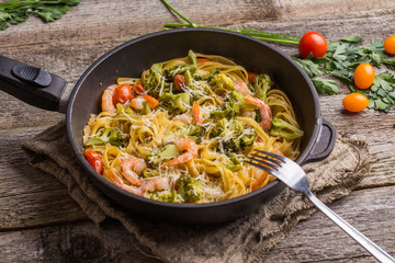 Pasta linguine with shrimps and broccoli in dripping pan on wooden background.