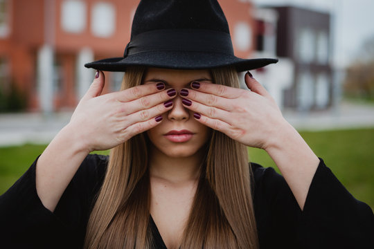Girl with a hat covering her face with the hands