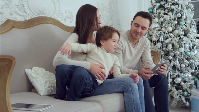 Young mom playing with her energetic little son while dad using tablet