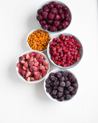 Organic frozen wild berries in bowls on white background.Ripe black currant, viburnum, buckthorn, cherries and wild strawberries

