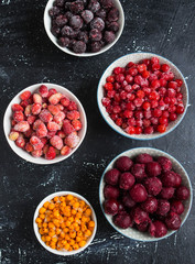 Various frozen berries in bowls. Black currant, sea buckthorn, cherry, strawberry, cranberry. Dark background.


