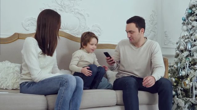 Happy family with their son sitting on the sofa while dad surfing on the phone