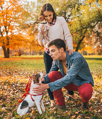 Happy young couple with dogs playing outdoors in autumn park