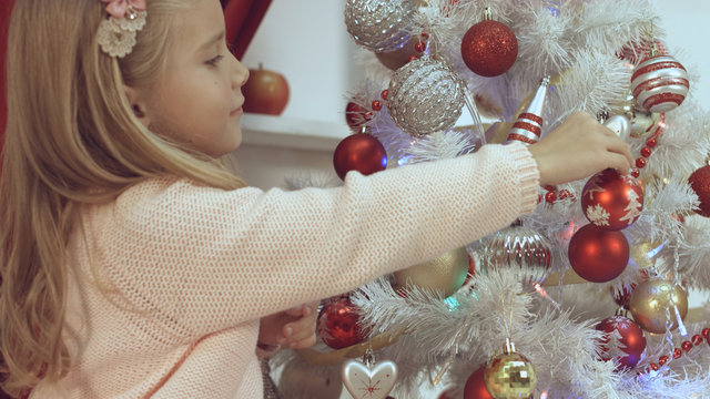 Little girl decorates the Christmas tree with toys