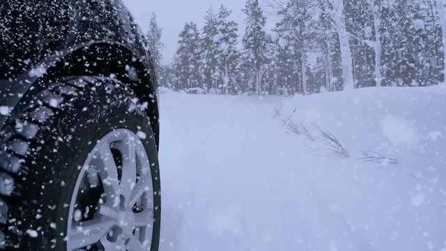 Winter. Road in the forest and lots of snow. Heavy snowfall and front tire of the car