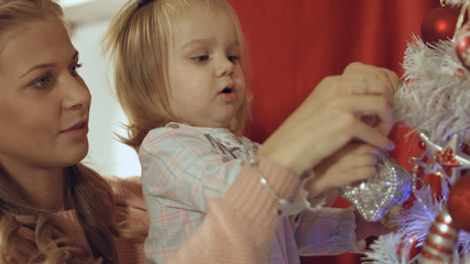 Mother with a small daughter decorate a festive Christmas tree