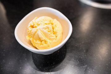 Scoop of vanilla ice cream in white bowl on black table with copy space.