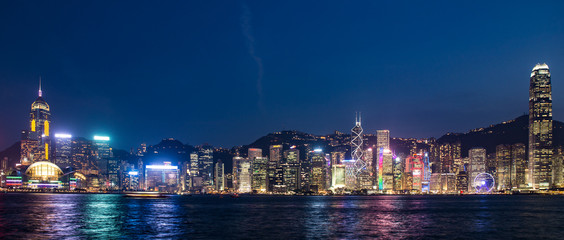 Obraz premium ​Hong Kong, China skyline panorama from across Victoria Harbor. Hong Kong city skyline view from harbor with skyscrapers buildings reflect in water at sunset