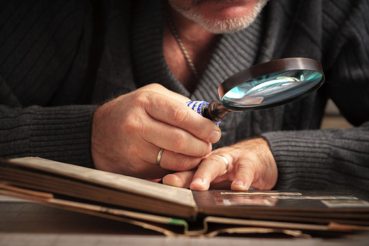 Man considers album of stamps trough the magnifying glass horizontal