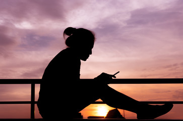 Side view of young girl using mobile phone in the sunset sky