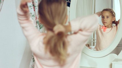 Fashionable little lady combing her hair and looking in the mirror