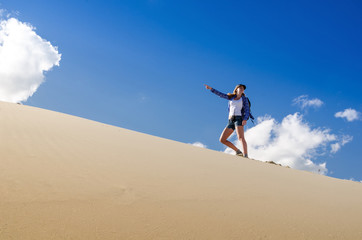 Young beautiful woman backpacker traveling in the desert. Sandy dunes and blue sky on sunny summer day. Travel adventure freedom concept.