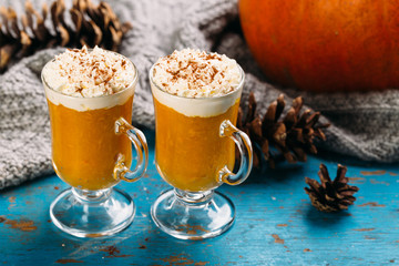 Pumpkin spiced latte or smoothie with whipped cream in glass on blue background Autumn or winter hot drink.