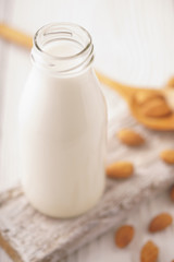 Almond milk in a glass bottle and almond nuts on a stand