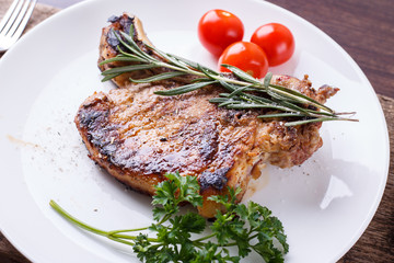 Grilled rib steak with rosemary and tomatoes on white dish
