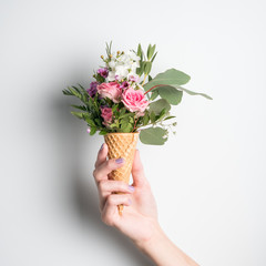 Beautiful flower in ice cream cone in girls hand with manicure on white background