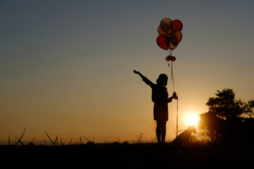Silhouette Girl with dog holding balloons watching the sunset.