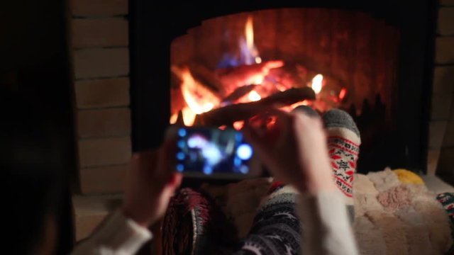 Girl resting by the fireplace and makes selfie on smartphone