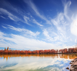 Scenic lake with autumnal forest along the shore and blue cloudy