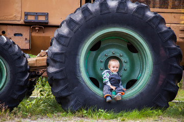 Little cute kid sitting in a huge wheel of the tractor. Wood mining machine.