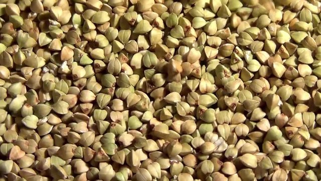Raw green buckwheat seeds rotating and falling, close up overhead view, healthy eco organic food