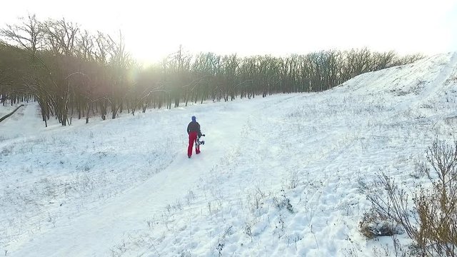 Snowboarder climbs up the hill in the forest at the sunny winter day. Slow motion. Aerial view.