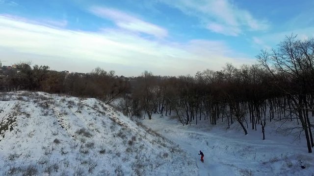 Snowboarder is riding downhill in the winter forest, at the quiet evening. Slow motion. Aerial view.
