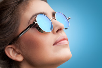 Close-up face portrait of young beautiful woman with perfect skin in round sunglasses looking up on blue background. Beauty face make-up.